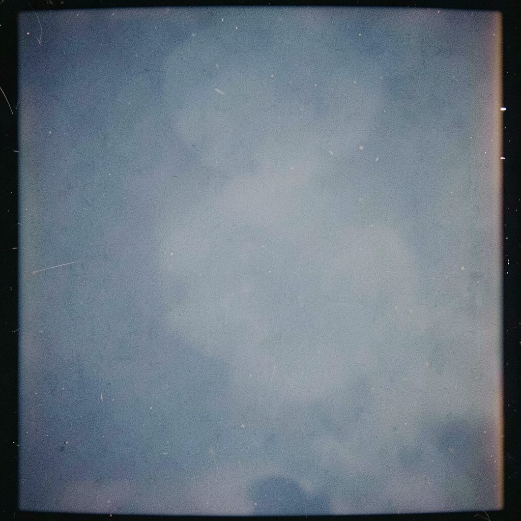 Muted blue-gray close-up of a polished dining table set with folded napkins, lit by gentle overhead light, in an analog film photograph with visible grain